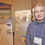 Lorne Peters stands in front of photos of early Manitoba Co-operative Honey Producers Ltd. members, including his father Pete Peters.