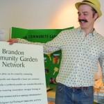 Blake Hamilton, organizer of the recent Seedy Saturday event, holds up a new multilingual sign that aims to remind Brandon’s community gardeners of the limits of charity.