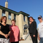 people standing outside an old schoolhouse