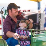 Richard Jackson and his son enjoy a ride on a 1947 John Deere under a umbrella during the daily parade.