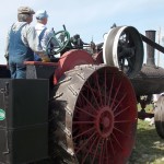 A near-century-old steam engine drives the belt powering the threshing unit.