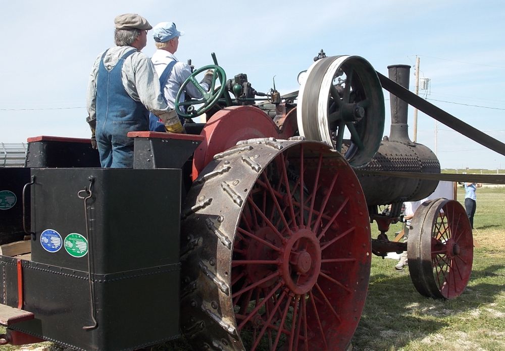 A near-century-old steam engine drives the belt powering the threshing unit.