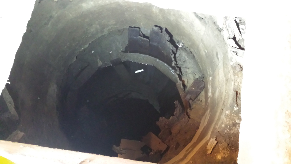 Looking into the well, the remains of the wood cribbing are visible. The concrete well head had collapsed leaving a void under the building foundation. &ensp;Photos: PVCD