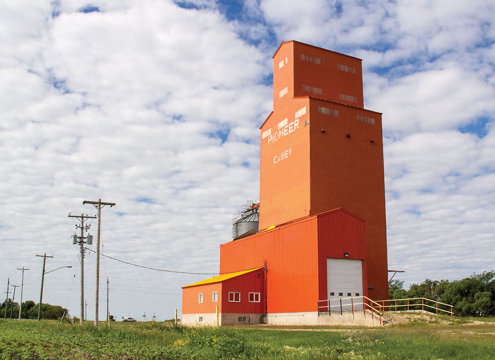 Two grain elevators at Carey, in the RM of De Salaberry, were owned by the Pioneer Grain Company, a subsidiary of James Richardson & Sons. Both have been demolished since the 1990s; this 2,620-tonne  elevator, painted in the bright-orange hallmark of the firm, came down in October 2014.