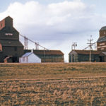 There were two chocolate-brown elevators at the Dutton Siding, on the CNR Togo Subdivision near Gilbert Plains, when this photo was taken in 1964. The UGG elevator at right had been built in 1920 and its annex was added in 1940. The left elevator was built by Paterson Grain before being sold in 1925 to Manitoba Pool. It was traded to UGG in late 1971. Between October and December 1976, both elevators were closed and later demolished.
