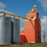 Several companies operated elevators at the railway siding of Glossop, near Strathclair, in the early days, including A. Forsythe & Company (1910s), Expert Elevator Company (1910s), Spencer Grain Company (1920s), and Western Grain Company (1930s-1940s). A wooden grain elevator that still stands, once owned by Western Grain, was acquired by Pioneer Grain when it bought the firm in 1952. Renovations included the replacement of its former red-brown colour with bright-orange paint. Around 2007, the elevator was sold to Parrish & Heimbecker who gave it the present white and black colour scheme. A wooden annex built by Pioneer on its west side, and two steel bins built for a neighbouring Manitoba Pool elevator on its east side, are now gone.