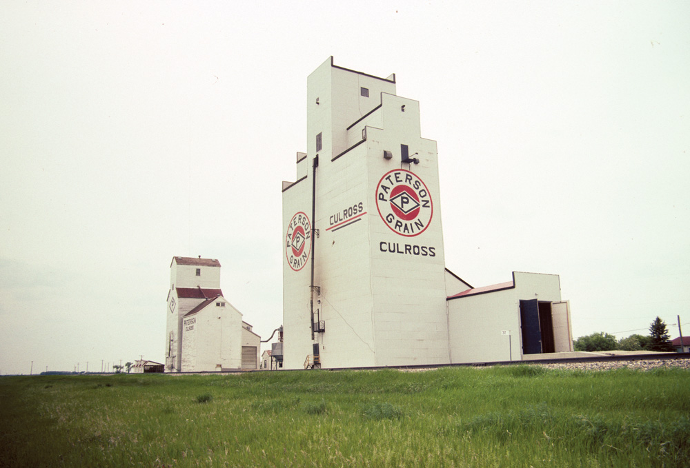 Two grain elevators at Culross, along Highway 2 in the Rural Municipality of Grey were in operation by the Paterson Grain Company when this photo was taken in July 1992. The elevator in the background, purchased from United Grain Growers in September 1969 (which bought it from Canadian Consolidated Grain in 1959), has since been removed. The other was moved here from nearby Elm Creek in February 1989. It is still in use by the company.