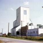 A grain elevator at Gladstone, shown here in 1969, held the double distinction of being the oldest country elevator in Manitoba made of concrete, and the first one to be demolished. Built in 1918 as a grist mill for the Echo Flour Mills Company, the mill portion was badly damaged by fire in 1919 but its grain elevator was left intact. The former mill building was used as a creamery until 1974 while the elevator was leased successively by Paterson Grain (1920-26), Manitoba Pool (1926-32), and United Grain Growers (1932-40). In July 1940, UGG purchased it outright. The facility closed in 1997.
