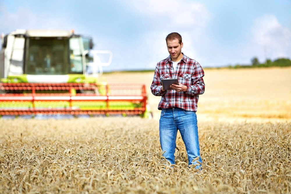Farmer Types on tablet computer with combine in the background