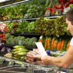 Young man reading shopping list in produce aisle, side view, close-up