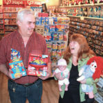 Jake Suderman holds the musical jack-in-the-box and spinning top initially bought for their young son. Classic toy purchases eventual led to selling toys in the Village Toy Shop on their property in Chortitz.  Helen Suderman holds some of the Village Toy Shop's most popular dolls.