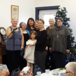 Bev Bennett (with microphone), back row (l to r), Julie McCahon, Janice Hunt, Dianna Airey, Wilma Bell, Wenda Best, present a cheque to Stacey Grocholsky and her daughter Kennedy.