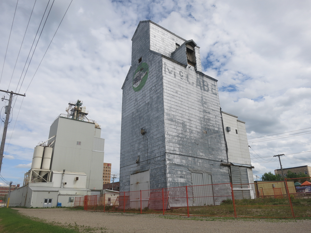 The history of ownership of this grain elevator, along Pacific Avenue in Brandon, is illustrated on its four sides. It was built around 1937 for the McCabe Brothers Grain Company, as shown by the name on its west  side. In 1965, the company erected six steel grain tanks and a feed-processing mill immediately east of the elevator. McCabe sold its elevators to United Grain Growers in early 1968 but this facility was excluded from the deal. Later that year, McCabe’s remaining assets were purchased by National Grain, named on its east side. The elevator (and the nearby mill) was bought in 1974 by Cargill, whose corporate signage is displayed on its north and south sides. At one time served by a spur line of the Canadian Pacific Railway that ran along its north side, there is no longer any rail service. Although slated for demolition in early 2016, it was still standing when this photo was taken in June 2016.