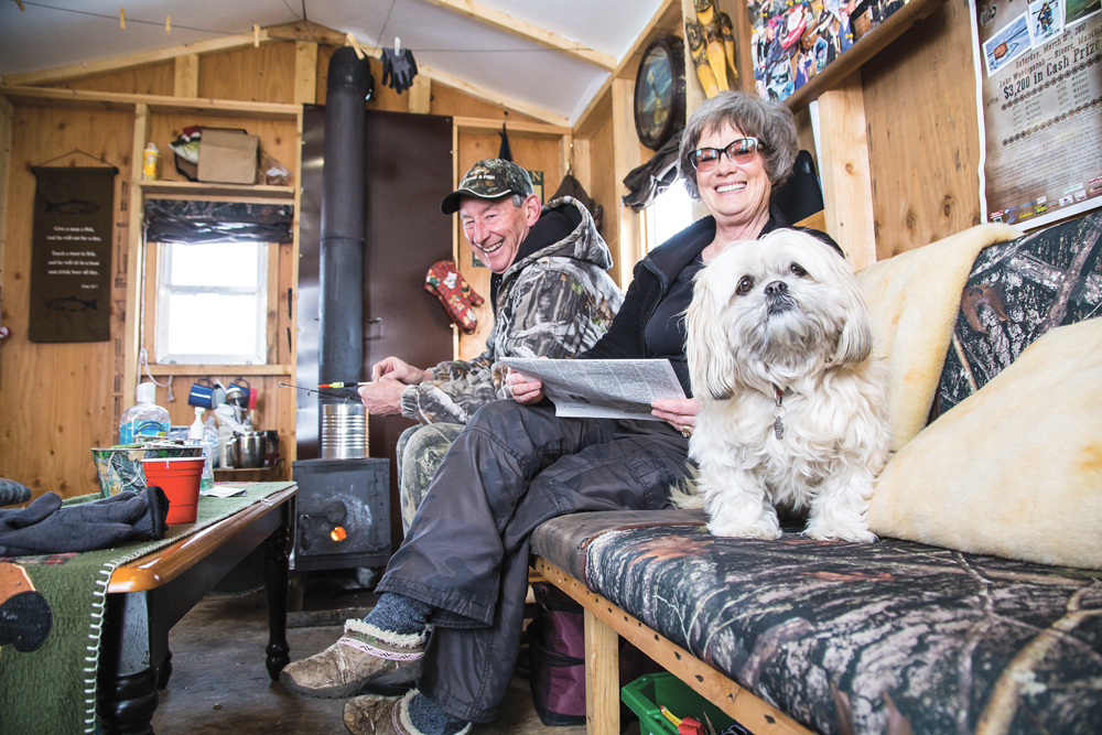 Ron Taylor of Rivers prepares a line as his wife Bonnie works on a crossword puzzle and their dog Delila keeps a watchful eye on the photographer all in the comfort of their ice fishing hut. The Taylors have participated in all 10 of the fish derbies.