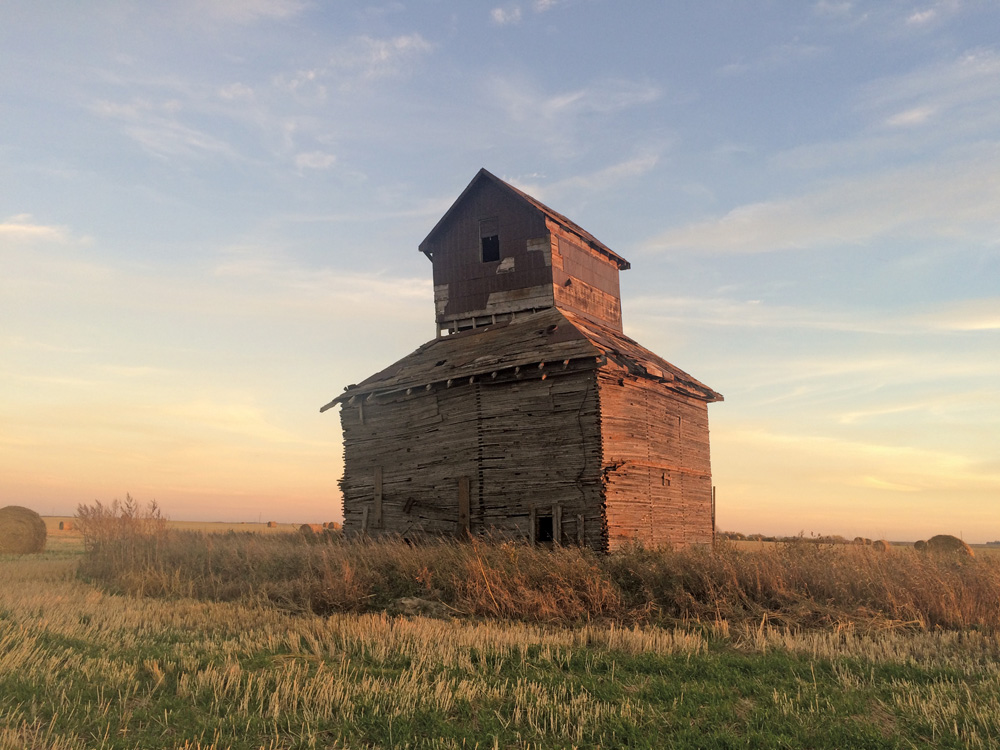 A small, wooden elevator in a field east of highway No. 242, south of La Riviere, is thought to have been built in the 1890s by Diggory Windsor and his brothers. It stood in their farmyard along with a brick house and shanty barn. A stationary engine and flywheel attached via the north side of the elevator drove its leg. The cupped belt lifted the grain to one of five bins, each holding about 1,200 bushels. By the 1970s, an external auger was used. Around 1979, the owner stopped using the elevator because its capacity was too small. It is slated for demolition due to concerns about rotten wood in its north wall.