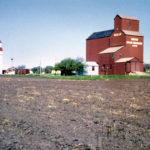 Around 1903, Western Canada Flour Mills built a 25,000-bushel elevator at Neelin, on the newly built CNR Wakopa Subdivision through the Rural Municipality of Argyle. In 1928, it was joined by a 30,000-bushel elevator constructed by United Grain Growers. By the time of this 1964 photo, the Western Canada elevator had been sold to Manitoba Pool, in 1940, and had been converted into an annex for a new elevator built in 1956. The mid-1950s also saw the addition of a 51,000-bushel crib annex beside the UGG elevator. Elevator and annex were traded to Manitoba Pool in 1973. Closed by December 1978, when the railway line was abandoned, the elevators have been removed from the site.