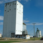A steel-reinforced concrete grain elevator in Swan River, the first such structure in Western Canada, was constructed for Searle Grain by the Gertz Construction Company of Winnipeg. It replaced an earlier wooden elevator. Standing 130 feet high, its 31 bins provided a total capacity of 100,000 bushels. The elevator opened officially on November 29, 1961. Repainted in 1966 following the merger of Searle with Federal Grain, it was painted again six years later when it was purchased by Manitoba Pool, becoming its fourth elevator at this point. Major renovations were made between 1975 and 1976, and a 24-bin wooden crib annex built in 1950, formerly attached to the Pool A, was moved beside it in 1982. The entire complex was demolished sometime between 2006 and 2013. Does anyone know the exact year?