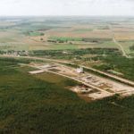 The former Manitoba Pool elevator site at The Pas seems literally carved out of the forest in this aerial view from the mid-1990s. Built on the outskirts between 1993 and 1994 to replace a 46-year-old wooden elevator in town that had been purchased from Federal Grain in 1972, this 80,000-bushel, four-bin facility featured all-steel construction and two 4,500-bushel/hour legs. Opened officially in October 1994, it closed almost exactly 14 years later with Viterra officials citing “limited storage and throughput capacity” that made it uneconomical. The elevator was demolished in 2014.