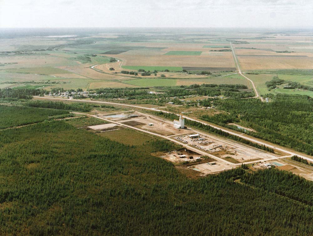 The former Manitoba Pool elevator site at The Pas seems literally carved out of the forest in this aerial view from the mid-1990s. Built on the outskirts between 1993 and 1994 to replace a 46-year-old wooden elevator in town that had been purchased from Federal Grain in 1972, this 80,000-bushel, four-bin facility featured all-steel construction and two 4,500-bushel/hour legs. Opened officially in October 1994, it closed almost exactly 14 years later with Viterra officials citing “limited storage and throughput capacity” that made it uneconomical. The elevator was demolished in 2014.
