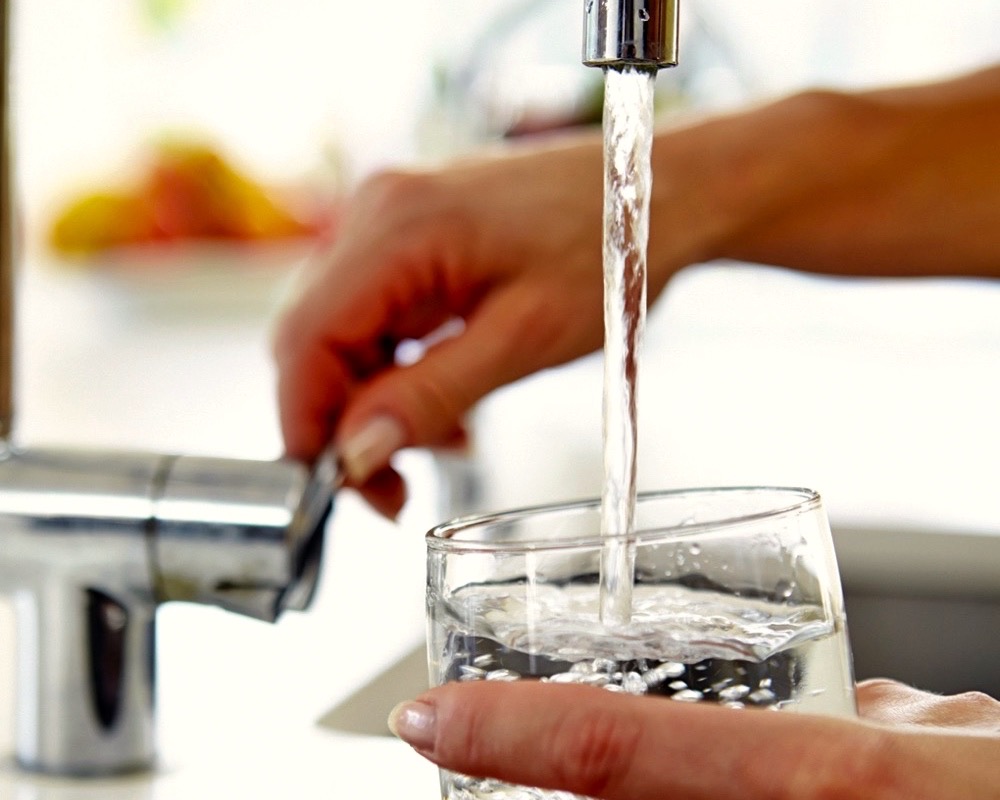 Woman Pouring Glass Of Water From Tap In Kitchen