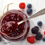 Jar of wild berry jam on white wooden background from top view