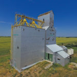 A 40,000-bushel grain elevator in Clanwilliam, in the RM of Minto-Odanah, was built in 1928 and operated by a co-operative association affiliated with Manitoba Pool. By the 1960s, it had a balloon annex on one side and an older, smaller elevator on the other. In 1982, the elevator was fully modernized, the balloon annex was removed, and a new crib annex replaced the old elevator. Closed in April 1996 when the CNR Rossburn Subdivision was abandoned, the facility has not been used for several years. As this recent photo shows, its metal cladding is damaged in several places and the exposed wood is deteriorating.