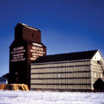 A 35,000-bushel wooden elevator at Kelwood, on the CNR Neepawa Subdivision in the Rural Municipality of Rosedale, was built in 1929 for Western Canada Flour Mills. In August 1940, it was taken over by the newly-formed Kelwood Co-operative Elevator Association. Initially handling just grain, the Co-operative began to sell coal in 1950 and farm supplies such as fertilizer, pesticide, and baler twine in 1963. A balloon annex was built beside it in 1969, increasing its capacity to 68,300 bushels. The facility was closed in December 1971, shortly before this photo was taken, and traded to United Grain Growers which, in turn, closed it in December 1979. The elevator and annex were sold to the community, along with UGG's other elevator built in 1927. Both elevators were removed from the site sometime before 2000. Does anyone know when?