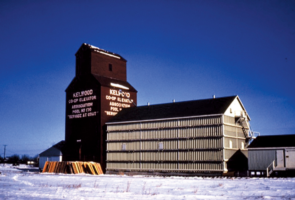 A 35,000-bushel wooden elevator at Kelwood, on the CNR Neepawa Subdivision in the Rural Municipality of Rosedale, was built in 1929 for Western Canada Flour Mills. In August 1940, it was taken over by the newly-formed Kelwood Co-operative Elevator Association. Initially handling just grain, the Co-operative began to sell coal in 1950 and farm supplies such as fertilizer, pesticide, and baler twine in 1963. A balloon annex was built beside it in 1969, increasing its capacity to 68,300 bushels. The facility was closed in December 1971, shortly before this photo was taken, and traded to United Grain Growers which, in turn, closed it in December 1979. The elevator and annex were sold to the community, along with UGG's other elevator built in 1927. Both elevators were removed from the site sometime before 2000. Does anyone know when?
