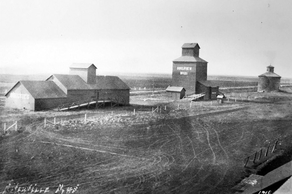 This historically significant photo of Niverville was taken in 1910, when three generations of grain-handling facilities were standing together. On the right was the first elevator in Western Canada, a round 25,000-bushel facility built in 1878 by William Hespeler of Winnipeg, to receive grain from newly arrived Mennonite farmers. On the left is a “flat” grain warehouse, a horizontal type that was once common across the Prairies. They were quickly replaced by more efficient vertical elevators. This one was used as a community hall from 1929 to 1963. In the centre is a 27,000-bushel elevator built in 1904 by Ogilvie Flour Mills and dismantled in 1938 to make way for a new 35,000-bushel elevator.