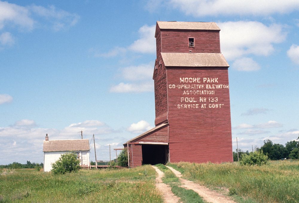 A 30,000-bushel elevator in Moore Park, in what is now the RM of Minto-Odanah on the former CPR Varcoe Subdivision, was built in 1929 by Manitoba Pool for a local association. It closed in July 1978 when the rail line was abandoned. By the time this photo was taken in July 1989 by Brandon University geographer John Everitt, the elevator had been vacant for years. Gone was a balloon annex from 1951 that had doubled its capacity. Also gone was a second, smaller elevator that stood behind this one. Built in 1905 by the Lake of the Woods Milling Company, it was acquired by Pool in 1960 as its “B” elevator. It closed in July 1978 too and was demolished in 1981. The Pool “A” elevator stood until at least the mid-1990s but has been removed from the site.