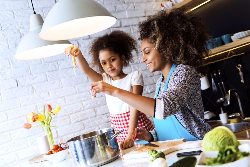 Beautiful African American woman and her daughter cooking in the kitchen