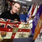 Shayne Campbell, executive director of the museum displays one of the flags received from Bishop Spence — a British Empire flag from a 1924 event in London, England. The flag has symbols of countries including India, Australia, Canada and New Zealand.