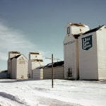 We see three elevators in this 1972 view of Fannystelle, all now gone. At left is Manitoba Pool with two annexes. Built in 1929, the balloon annex (left) dates from 1950 and a crib annex (right) was added in 1958. The smaller elevator in the middle was built in 1927 by Canadian Consolidated Grain, sold to UGG in 1959, closed in 1980, and removed in 1981. The small balloon annex (right) was built in 1949 and a crib annex (left) came in 1958. In 1970, the crib annex was moved beside the UGG elevator at right, which dates from 1940, built by Paterson Grain. Expanded in 1950 with a crib annex using materials salvaged from Dipple Siding, it was sold to UGG in 1968. UGG traded for the Pool in 1990 and closed both elevators that year when it opened a large concrete elevator nearby.