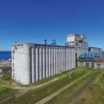 The Hudson Bay Railway reached Churchill in March 1929. One of the first priorities for construction was a terminal elevator for shipping grain to overseas markets. Designed by C. D. Howe & Company of Port Arthur (now Thunder Bay), it was erected by the Winnipeg firm of Carter Halls Aldinger between 1930 and 1931. A four-belt conveyor for loading up to four ships at once, at 20,000 bushels per hour, was completed in 1932. When done, the 2,500,000-bushel elevator was the second largest of its kind in the world. The 56 bins at its north (right) end, added between 1954 and 1955, doubled its capacity. Seen in this aerial view from June 2018, the elevator stands idle while the railway, damaged in May 2017, awaits repair.