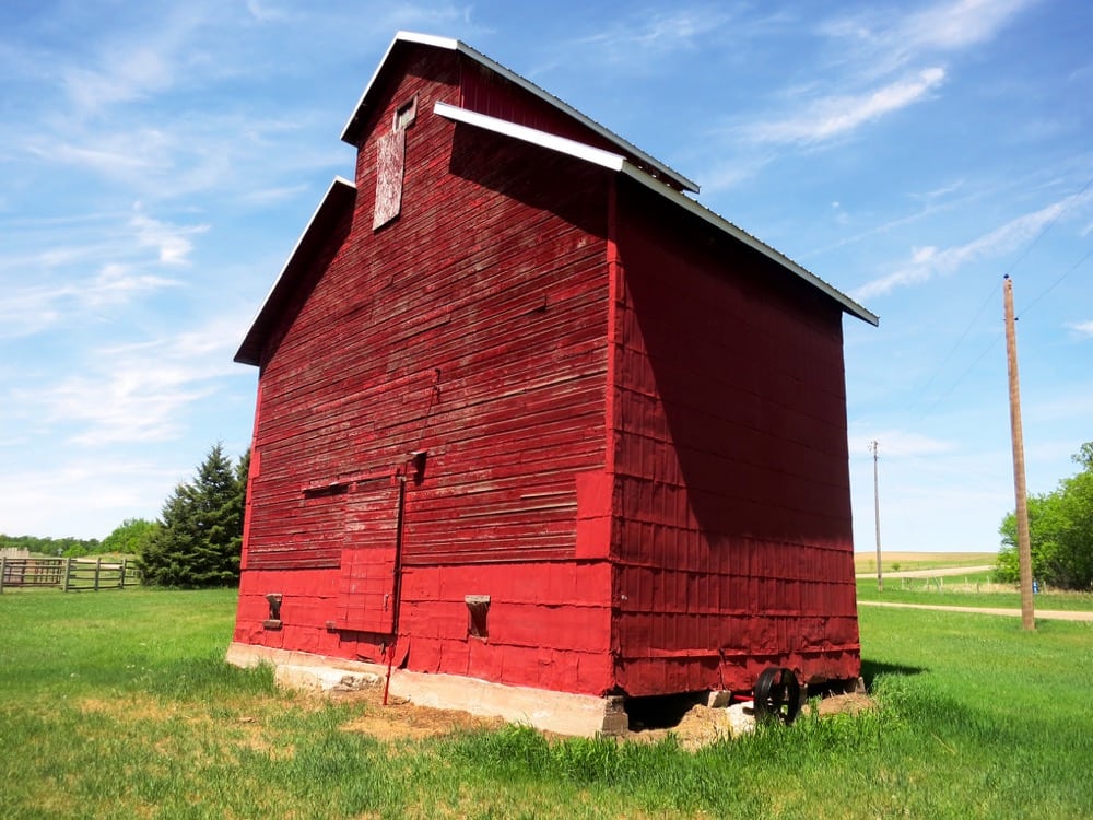 A small wooden-crib elevator in the Municipality of Norfolk Treherne, similar in design to Manitoba’s oldest elevator, at Elva, was built in 1901 by Irish immigrant William Twiss Grogan and his family. Local lore holds that it was built using lumber sawed from logs salvaged from a log-jam in the nearby Assiniboine River. It had four full-size bins and two half-bins. Sold to neighbour Alex Dobbin along with the surrounding land in 1911, the structure (seen here in May 2018) remains in good repair. It contains the original leg and is still used for grain storage by Dobbin’s descendants.