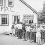 Young folk during a 1953 or 1954 camp lineup at the dining hall with the Manitoba Federation of Agriculture and Co-operation ‘MFAC’ sign over the entranceway.