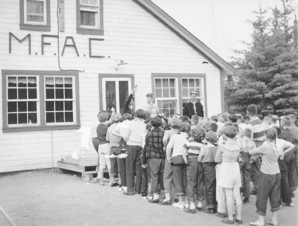 Young folk during a 1953 or 1954 camp lineup at the dining hall with the Manitoba Federation of Agriculture and Co-operation ‘MFAC’ sign over the entranceway. 