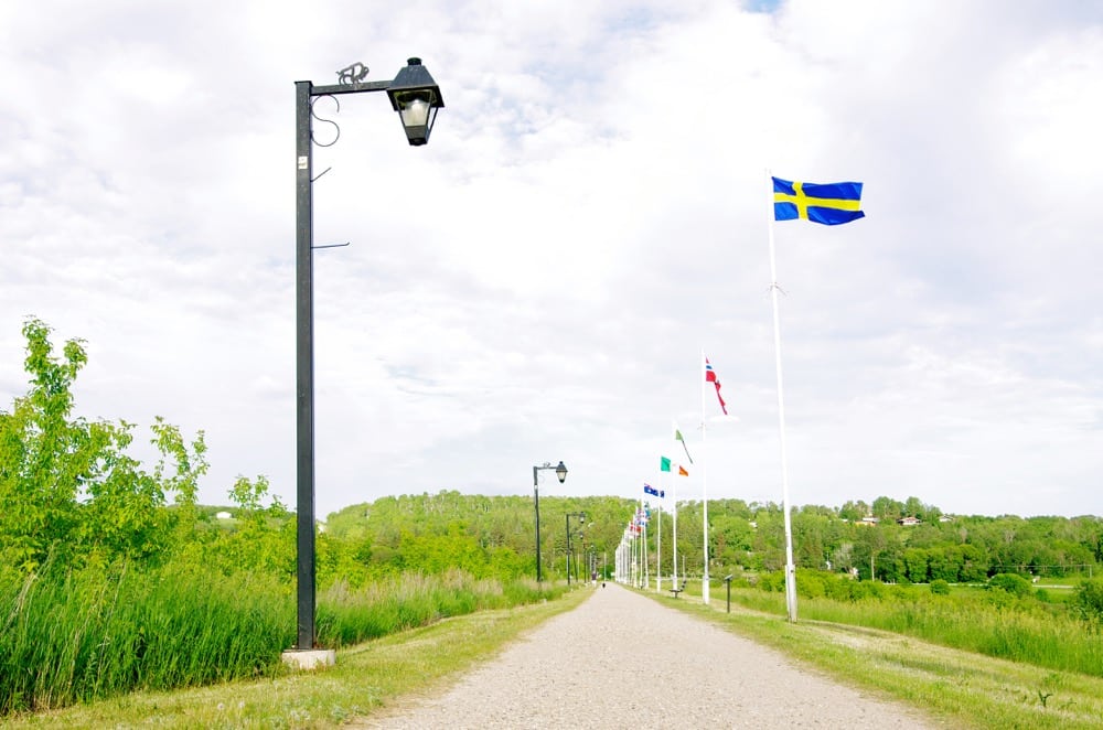 Flags from other countries, provinces and territories top Minnedosa's dam, alongside a walking path and historical interpretive signs.