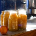 Jars of freshly applesauce with home-canning equipment in the background.