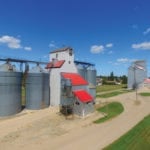 Two off-track elevators at Cypress River, seen in this photo from July 2018, are operated by Paterson Grain. The western (left) elevator was built in 1927 and expanded with balloon annexes in 1940, 1953, and 1963. The annexes were replaced by four steel tanks in the 1980s. The eastern (right) elevator was built in 1928 by Manitoba Pool. Its capacity was augmented with a balloon annex in 1954 and a crib annex in 1976. Closed by Agricore in 2001, it was sold to Paterson in 2004. Formerly serviced by the CPR Glenboro Subdivision, the line past the elevators was abandoned in September 2014 and the rails were removed in the summer of 2016.