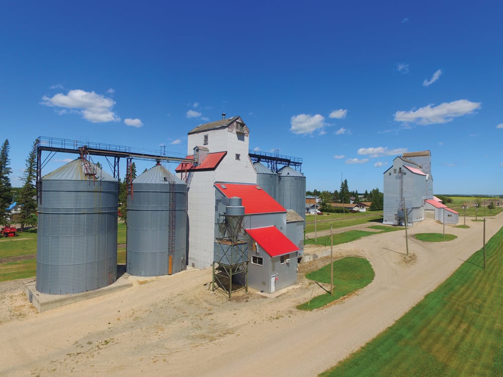 Two off-track elevators at Cypress River, seen in this photo from July 2018, are operated by Paterson Grain. The western (left) elevator was built in 1927 and expanded with balloon annexes in 1940, 1953, and 1963. The annexes were replaced by four steel tanks in the 1980s. The eastern (right) elevator was built in 1928 by Manitoba Pool. Its capacity was augmented with a balloon annex in 1954 and a crib annex in 1976. Closed by Agricore in 2001, it was sold to Paterson in 2004. Formerly serviced by the CPR Glenboro Subdivision, the line past the elevators was abandoned in September 2014 and the rails were removed in the summer of 2016.