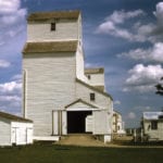 A United Grain Growers elevator at the railway siding of Cranmer, on the CPR line between Goodlands and Waskada, was built to replace an earlier one that collapsed suddenly in September 1928. It opened for business in 1929 and was expanded with a crib annex in 1954. Seen here in 1971, a second elevator in the background was built in 1927 by the Matheson-Lindsay Elevator Company and owned successively by the Province Elevator Company (1928) and Reliance Grain (1939) before being purchased by UGG in 1948. Both closed in December 1975 and were demolished.