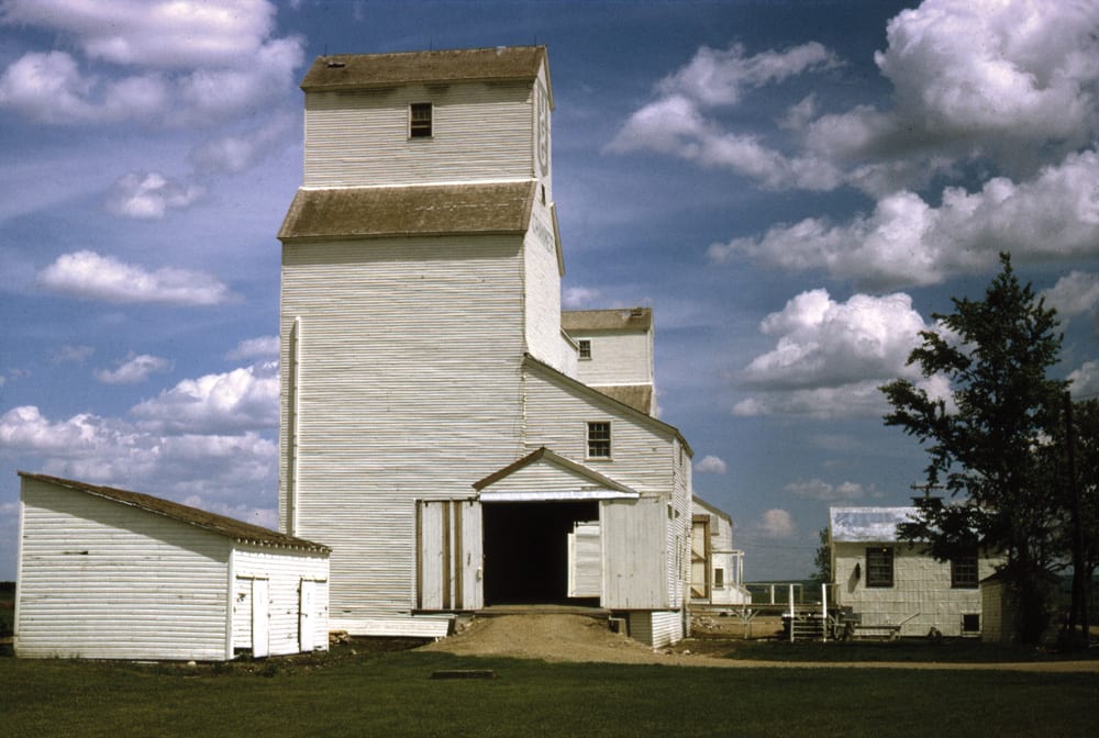 A United Grain Growers elevator at the railway siding of Cranmer, on the CPR line between Goodlands and Waskada, was built to replace an earlier one that collapsed suddenly in September 1928. It opened for business in 1929 and was expanded with a crib annex in 1954. Seen here in 1971, a second elevator in the background was built in 1927 by the Matheson-Lindsay Elevator Company and owned successively by the Province Elevator Company (1928) and Reliance Grain (1939) before being purchased by UGG in 1948. Both closed in December 1975 and were demolished.