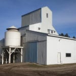 This seed-cleaning plant about five miles southeast of Notre Dame de Lourdes hardly looks like the elevator that lies at its core. Built by Federal Grain in 1936, to replace an elevator destroyed by fire in September 1935, it was closed in 1964 and sold to Gabriel Durand the following year. He removed a top portion of the crib to make it easier to move the nine miles to his farm then rebuilt the roof but not as high as the original. His son Marc continues to run the plant.