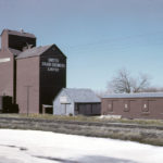 An elevator at Rosebank, along highway No. 23 between Miami and Roland, was built by United Grain Growers in 1927, replacing an earlier elevator at the site. Its initial capacity was 30,000 bushels but, in 1953, the facility was doubled by a crib annex constructed beside it. Seen here in 1962, the elevator was renovated in 1970, closed in 1988, and demolished in mid-1990.