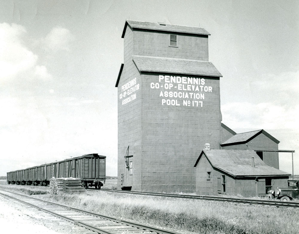 A small stone monument in the Municipality of Riverdale is all that marks the location of Pendennis. Established in 1903 and named for a character in the 19th century novel The History of Pendennis, this siding on the CPR Lenore Subdivision had a post office, general store, and Manitoba Pool elevator, seen in this photo from August 1948. The last vestige was gone by March 1964 when the elevator was destroyed by fire.