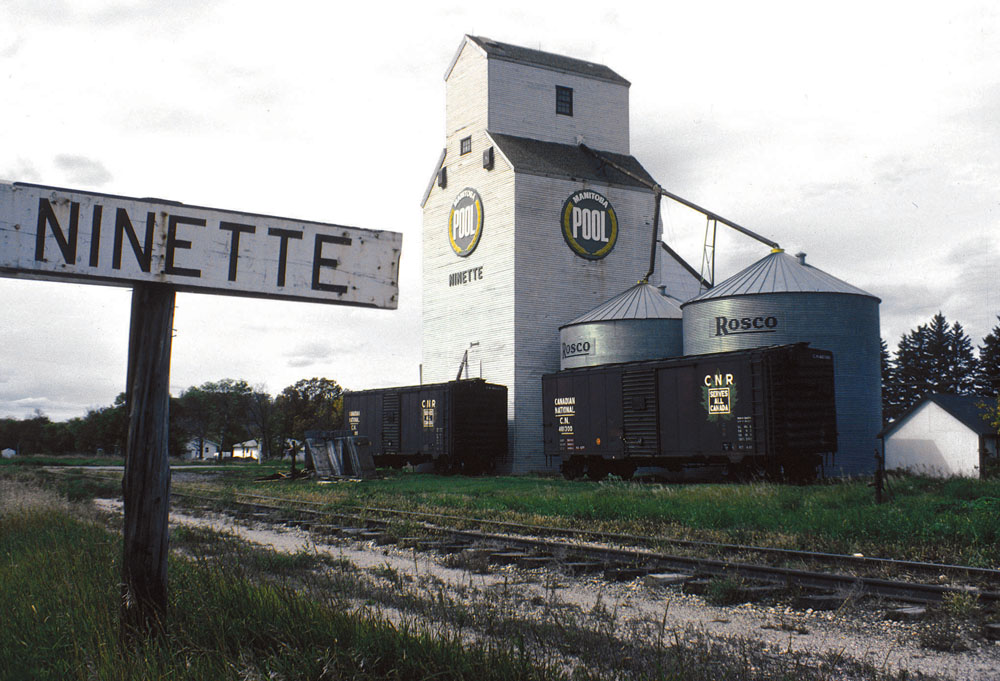The original Manitoba Pool elevator at Ninette burst open and collapsed in September 1967 and was replaced by one moved from nearby Hilton, acquired in trade from United Grain Growers. The relocated elevator was officially opened in December 1967, with the first unloading by John McKay, the last still-farming original member of the Ninette Pool Elevator Association. This photo of it dates from 1977. The elevator was closed in August 1987 and, despite efforts to save it, was demolished in late October 1988, with the debris burned at the local landfill.