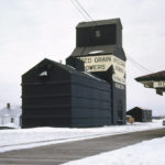 An elevator at Rorketon was built in 1924 by United Grain Growers. At the time of this 1962 photo, it had a balloon annex on one side and a small coal shed on the other, and stood across from the train station. UGG cited increasing costs of operation and impending abandonment of the CN rail line from Ste. Rose du Lac when it closed the elevator in August 1980.