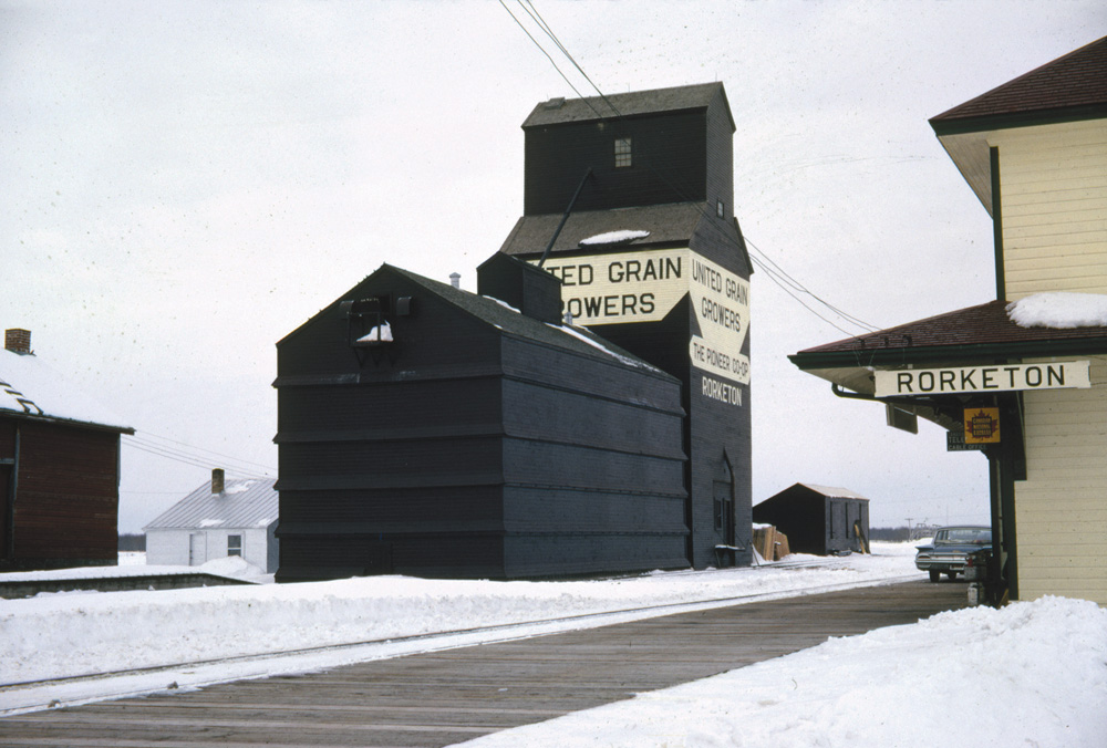 An elevator at Rorketon was built in 1924 by United Grain Growers. At the time of this 1962 photo, it had a balloon annex on one side and a small coal shed on the other, and stood across from the train station. UGG cited increasing costs of operation and impending abandonment of the CN rail line from Ste. Rose du Lac when it closed the elevator in August 1980.