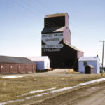 When this photo was taken in 1962, St. Claude had two United Grain Growers elevators. The older one, in the background, was built by Ogilvie Flour Mills around 1914. Sold to Manitoba Pool in 1959, it was traded to UGG the following year. The younger elevator in the foreground was built by UGG in 1927 to replace an earlier structure purchased from the provincial government. Also visible on the extreme left is a common fixture of many elevators in earlier days: a coal shed to supply local residents with this once-important, now obsolete heating fuel. Closed around 1991, both elevators have been gone for years.